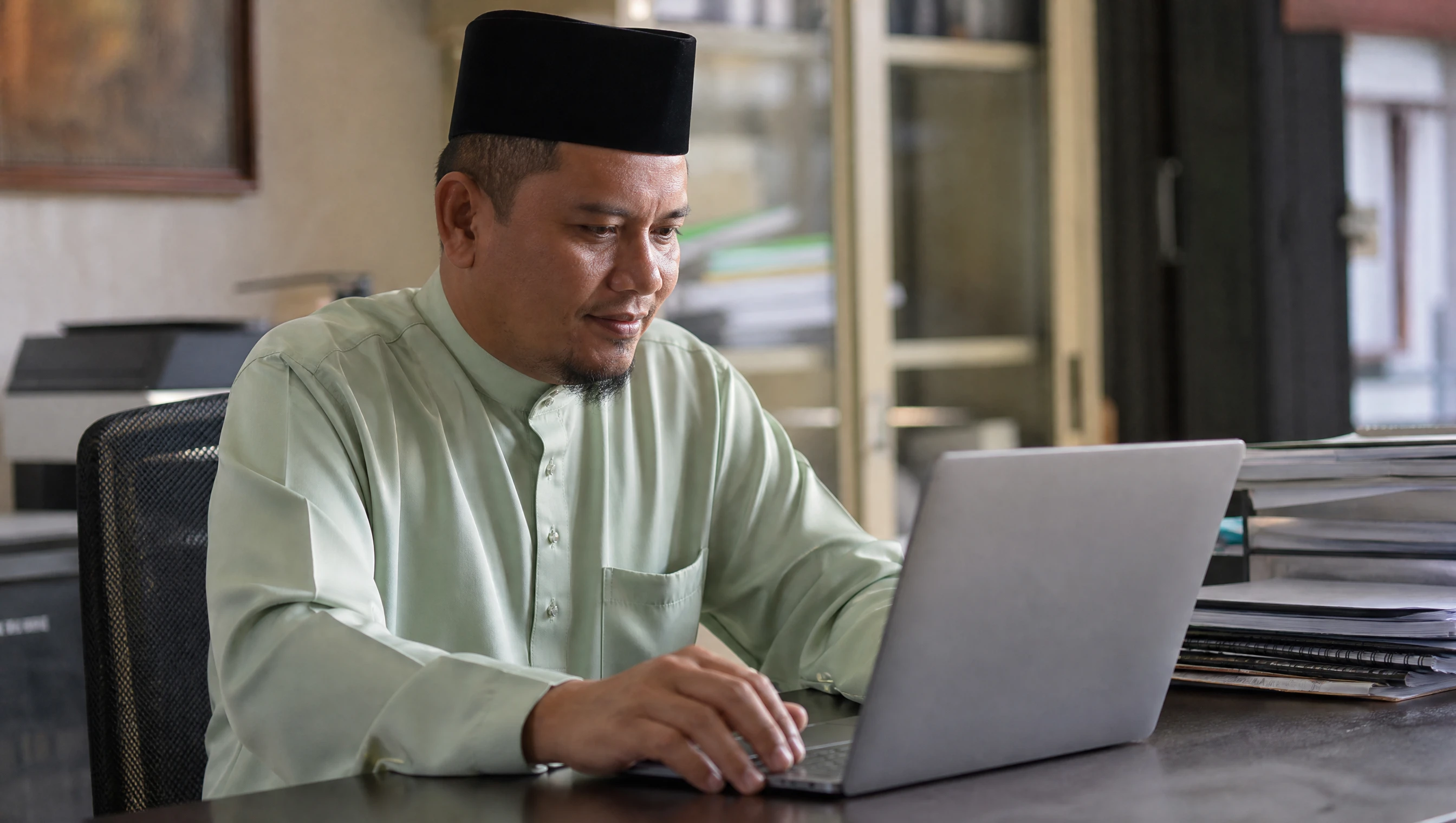Pemilik bisnes Melayu tengok website company profile syarikatnya di skrin laptop di pejabat kecil