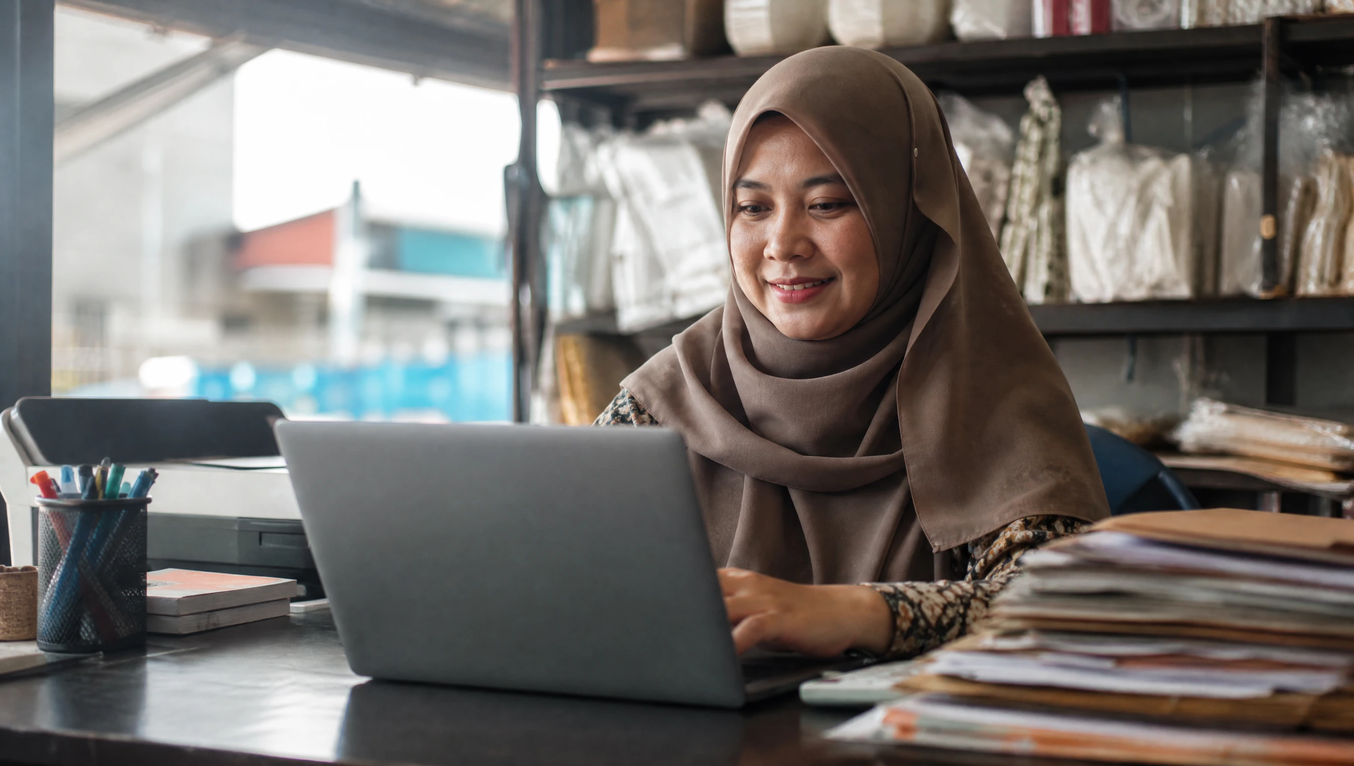 Malaysian business owner using a web management system on a laptop at her shop